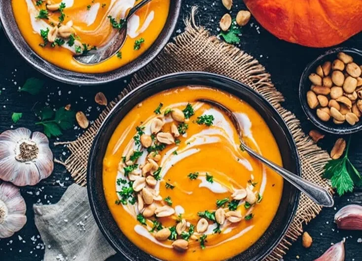 Cremige Kürbissuppe vegan in einer Schale mit frischen Kräutern garniert
