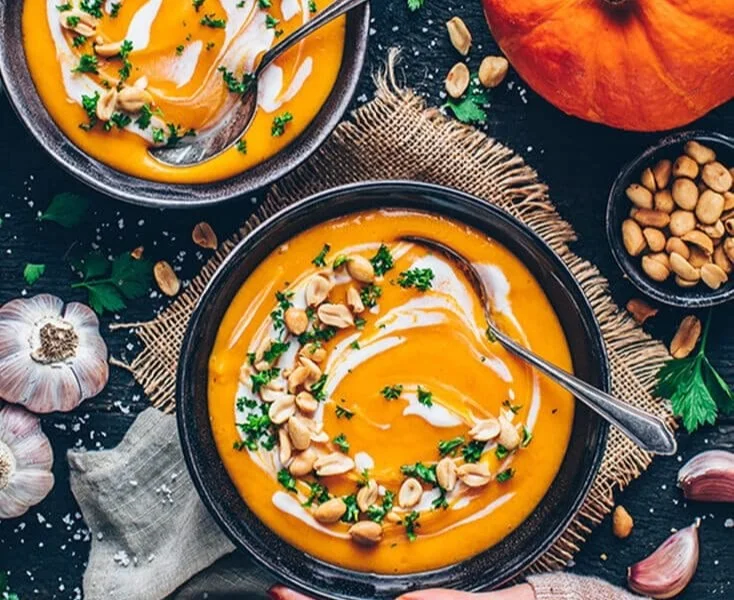 Cremige Kürbissuppe vegan in einer Schale mit frischen Kräutern garniert