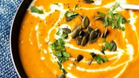 Schüssel mit einfacher Kürbissuppe mit Curry, dekoriert mit frischen Kräutern.