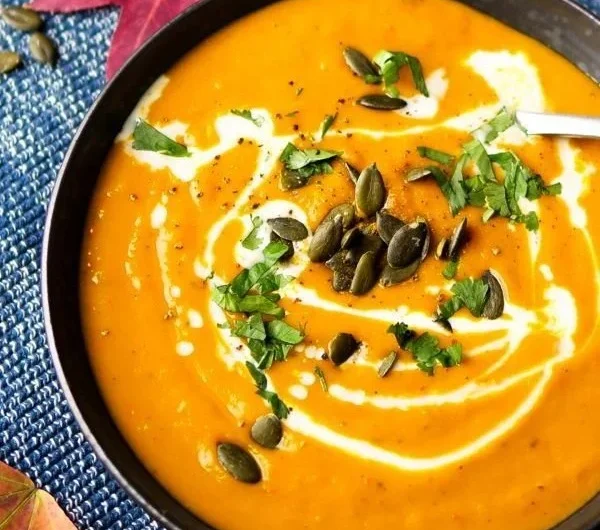 Schüssel mit einfacher Kürbissuppe mit Curry, dekoriert mit frischen Kräutern.