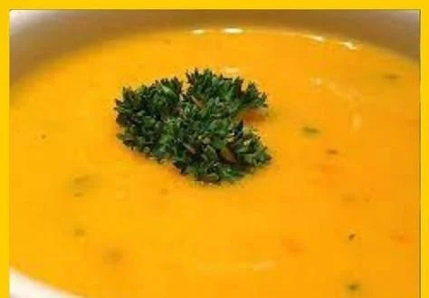 Schüssel mit Kürbis-Karotten-Suppe garniert mit frischen Kräutern