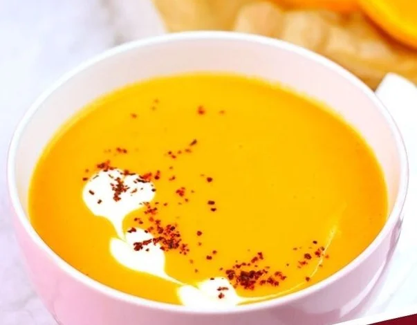 Kürbissuppe mit Kokosmilch in einer Schüssel, garniert mit frischen Kräutern.