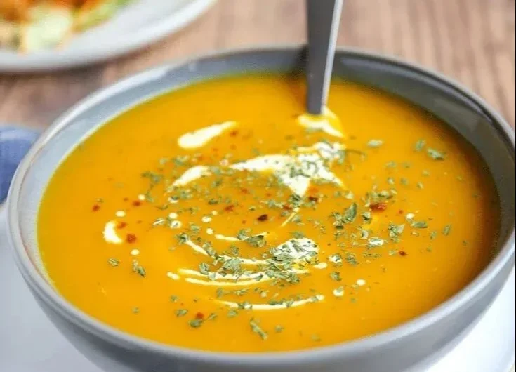 Würzige Karottensuppe in einer Schüssel mit frischen Kräutern garniert.