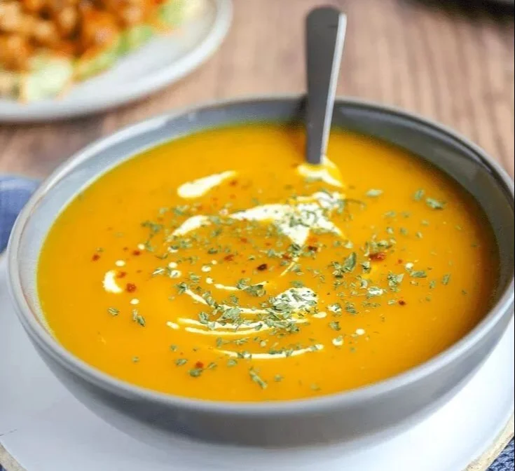 Würzige Karottensuppe in einer Schüssel mit frischen Kräutern garniert.