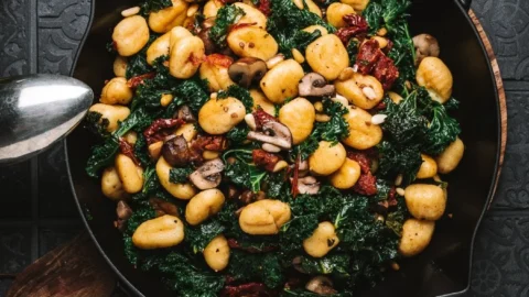 Gnocchi-Grünkohl-Pfanne mit Pilzen und getrockneten Tomaten auf einem Teller serviert.