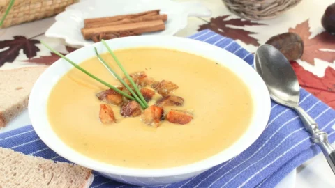 Schüssel Maronencremesuppe garniert mit frischen Kräutern und einer Beilage von Brot.