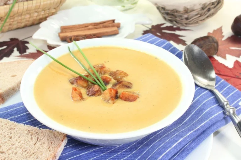 Schüssel Maronencremesuppe garniert mit frischen Kräutern und einer Beilage von Brot.