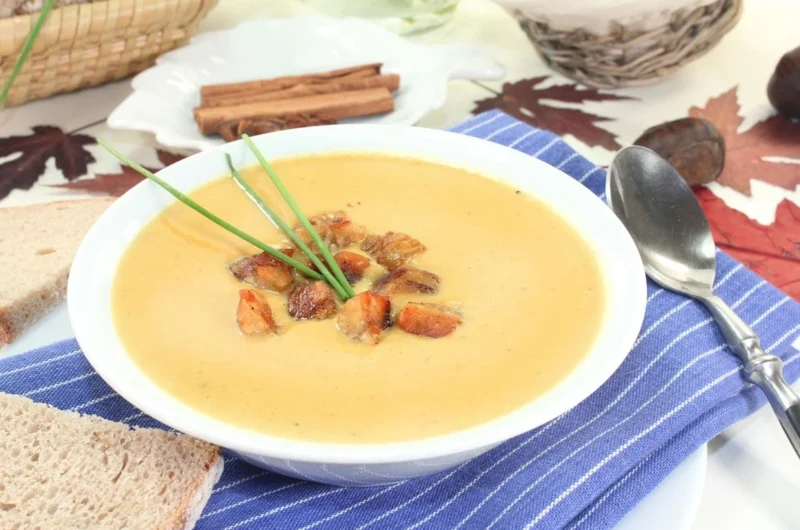 Schüssel Maronencremesuppe garniert mit frischen Kräutern und einer Beilage von Brot.